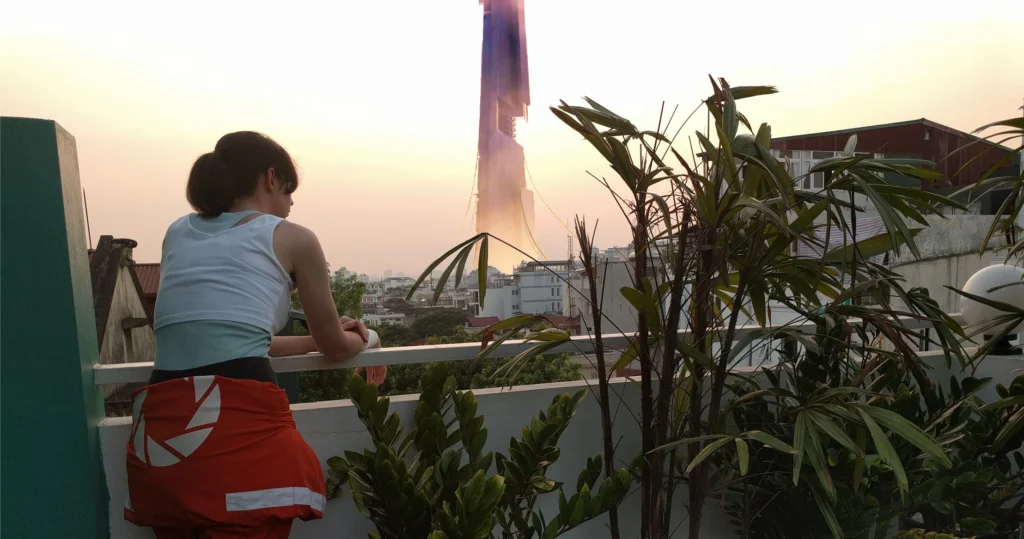 Un vieux photo montage réalisé avec Paint Dot Net, sur lequel on me voit de dos en cosplay de Chell de Portal 2 sur un balcon, avec au loin la citadelle de Cité 17 dans Half-Life 2 et le paysage urbain de Hanoï