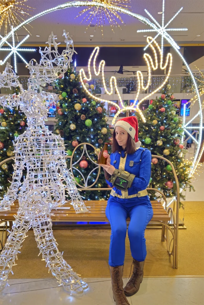 Je pose en costume de Fallout 4 avec un bonnet de Noël, aux côtés d'une créature fantastique illuminée en led et entourée de décorations de Noël