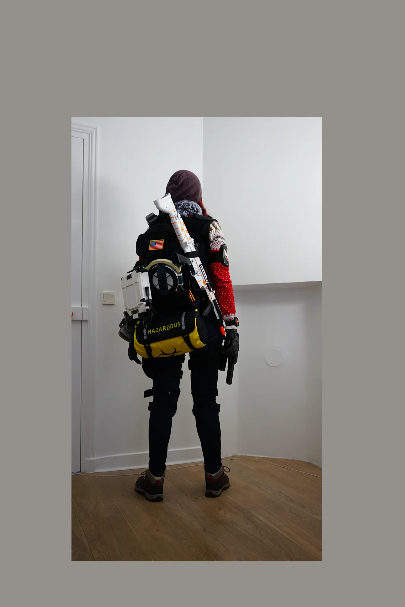 La photo de moi dans mon salon en cosplay d'agent de The Division, avec une réplique d'arme, une station de soutien et un module d'impulsion sur un sac à bandoulière classique du jeu, un sac d'objets contaminé, et un pull de Noël vif