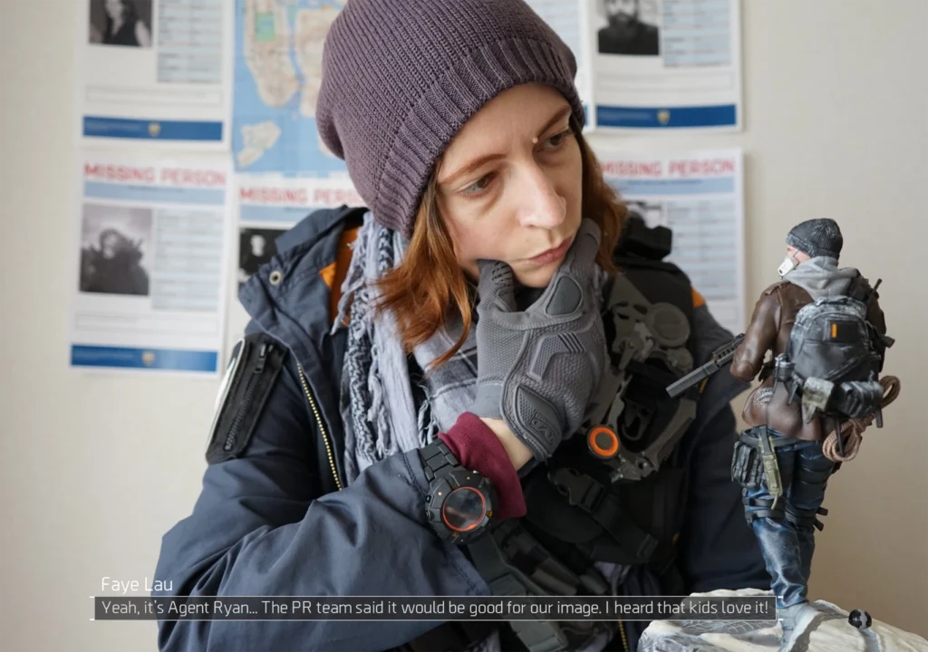 Une vue rapprochée de moi en cosplay de The Division regardant la figurine de l'agent Ryan, d'un air perplexe. Un texte dit : "Faye Lau : Oui c'est l'agent Ryan... La comm' a dit que ce serait bien pour notre image"